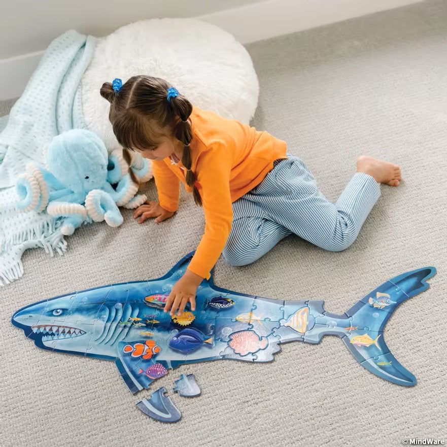 Fillette qui assemble le grand casse-tête Requin sur un tapis, avec des pièces en forme de poissons tropicaux